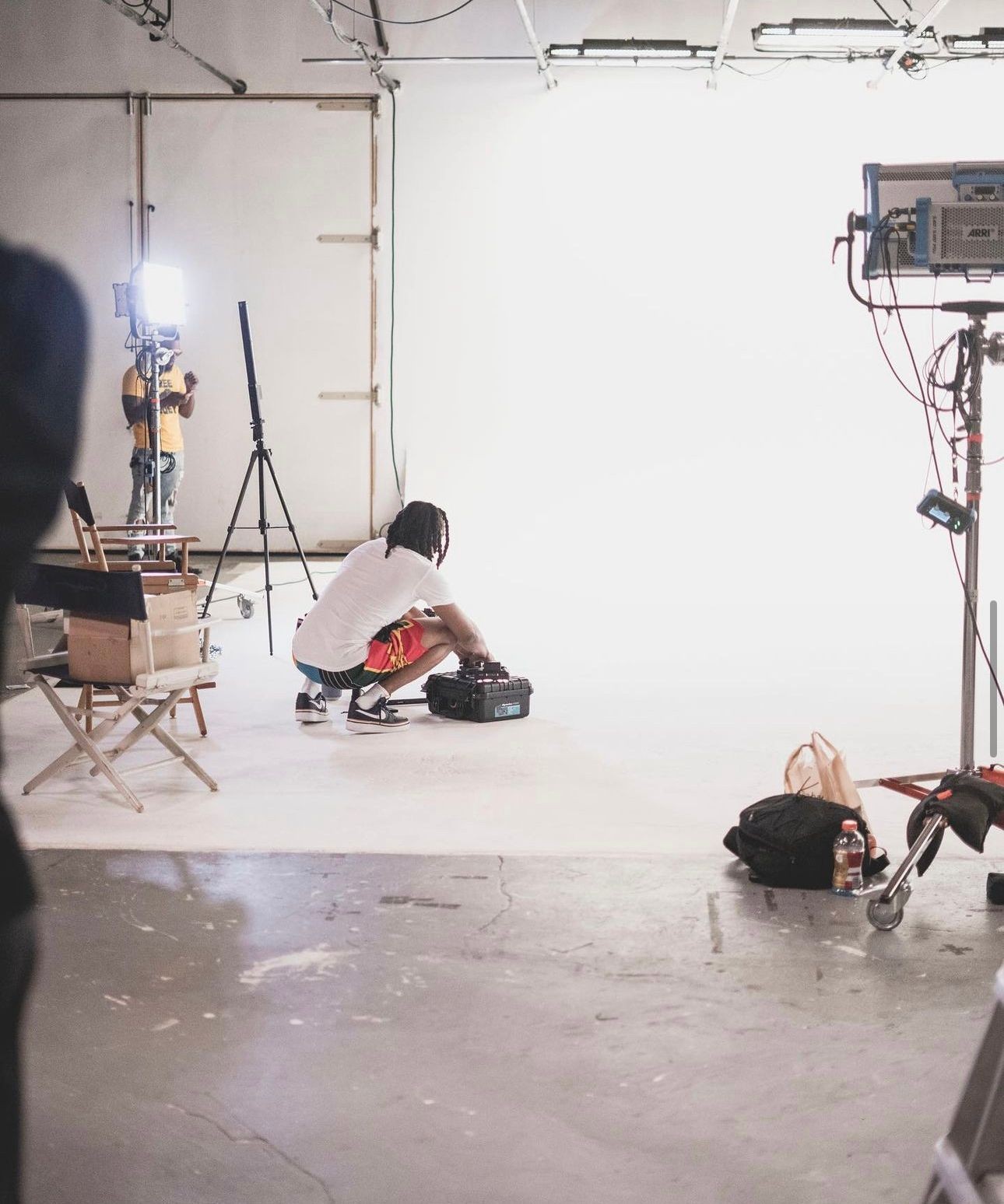 Person setting up equipment in a well-lit photography studio with camera gear and lighting.